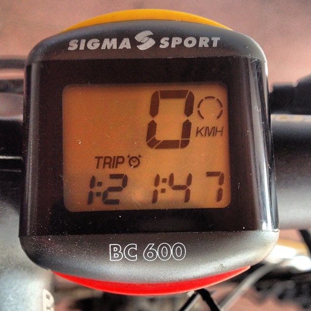 A photo of an old Sigma Sport bike computer attached to bike handlebars showing speed and trip time.