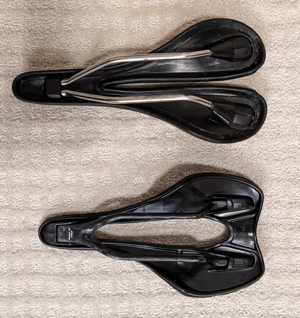 Photo of two Selle Italia bike saddles side by side, viewed from the bottom. An SLK Gel Flow with Vanox rails (on the top) and an SLR Boost Kit Carbonia Superflow size S3 (on the bottom).