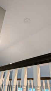 A photo of the ceiling of a residential house showing a Ubiquiti Unifi nanoHD Wi-Fi access point attached to the ceiling.