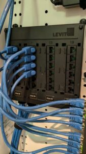 A photo of an CAT 6 RJ-45 punch-down block mounted in a structured media enclosure with eight blue ethernet cables connected.